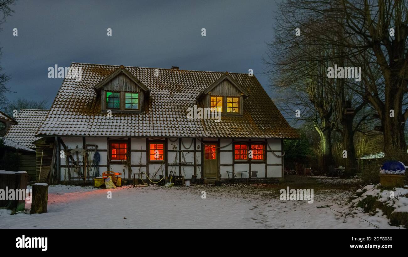 Fattoria illuminata in legno in una serata invernale innevata Foto Stock