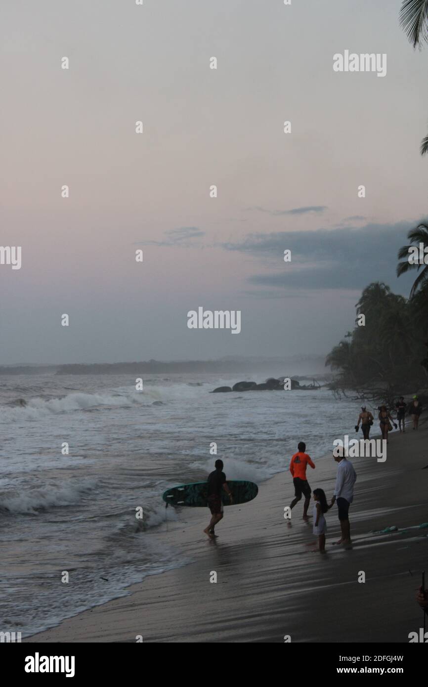 Tramonto in spiaggia con alcune persone che si godono il mare vibrazioni Foto Stock