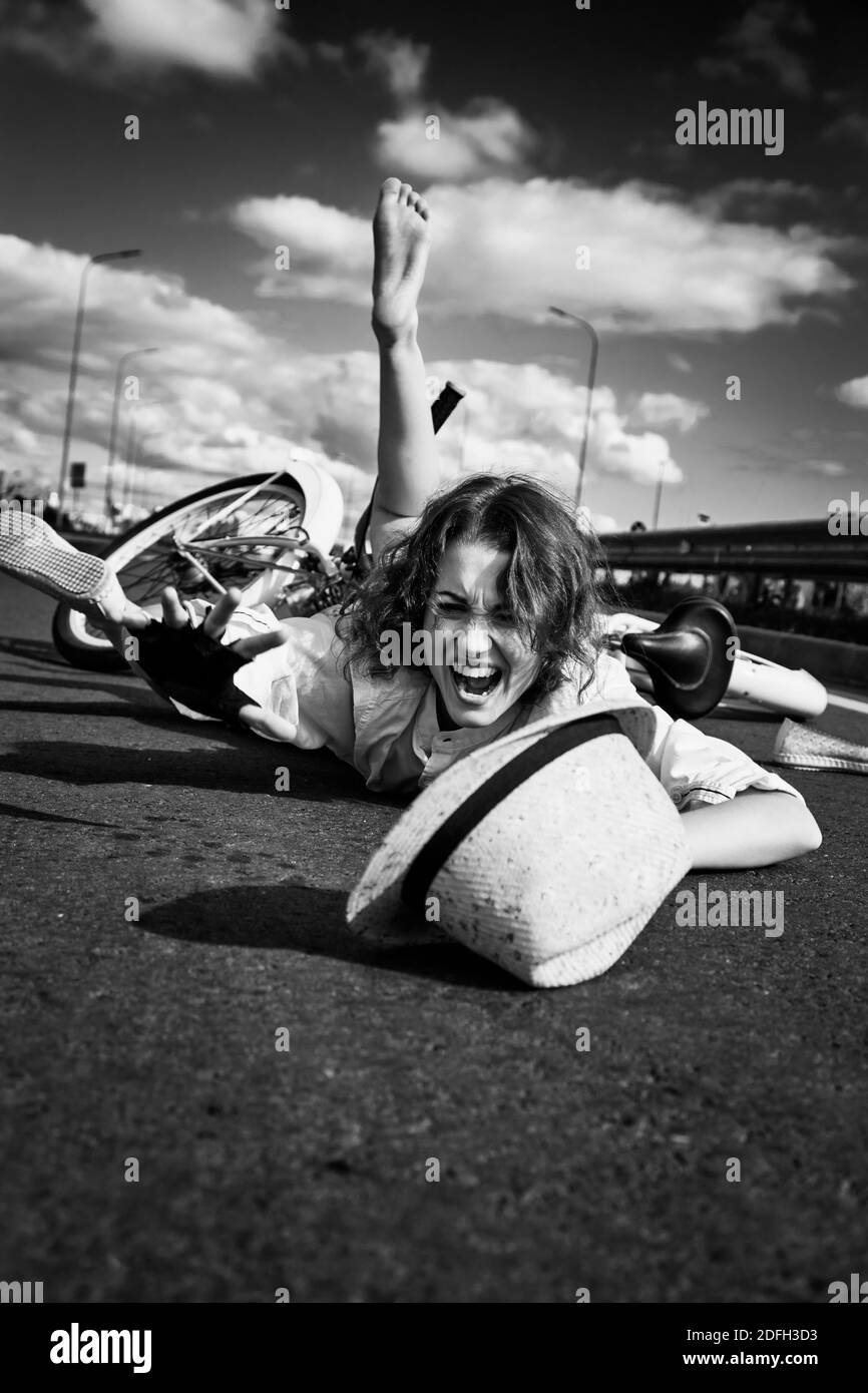 giovane donna cadde dalla bicicletta, giace su grida di asfalto, monocromatica Foto Stock