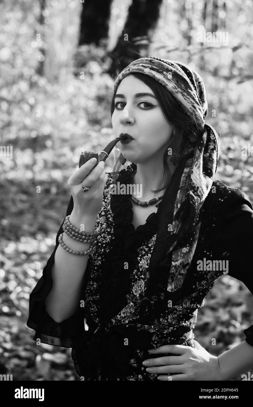 giovane donna gitana fumando tubo in autunno foresta, guardando fotocamera, monocromatico Foto Stock