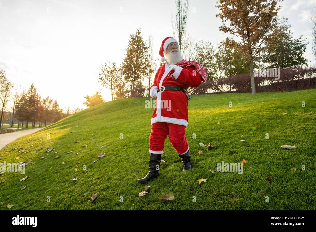 Divertente Babbo Natale che cammina lungo la strada con una borsa di regali Foto Stock