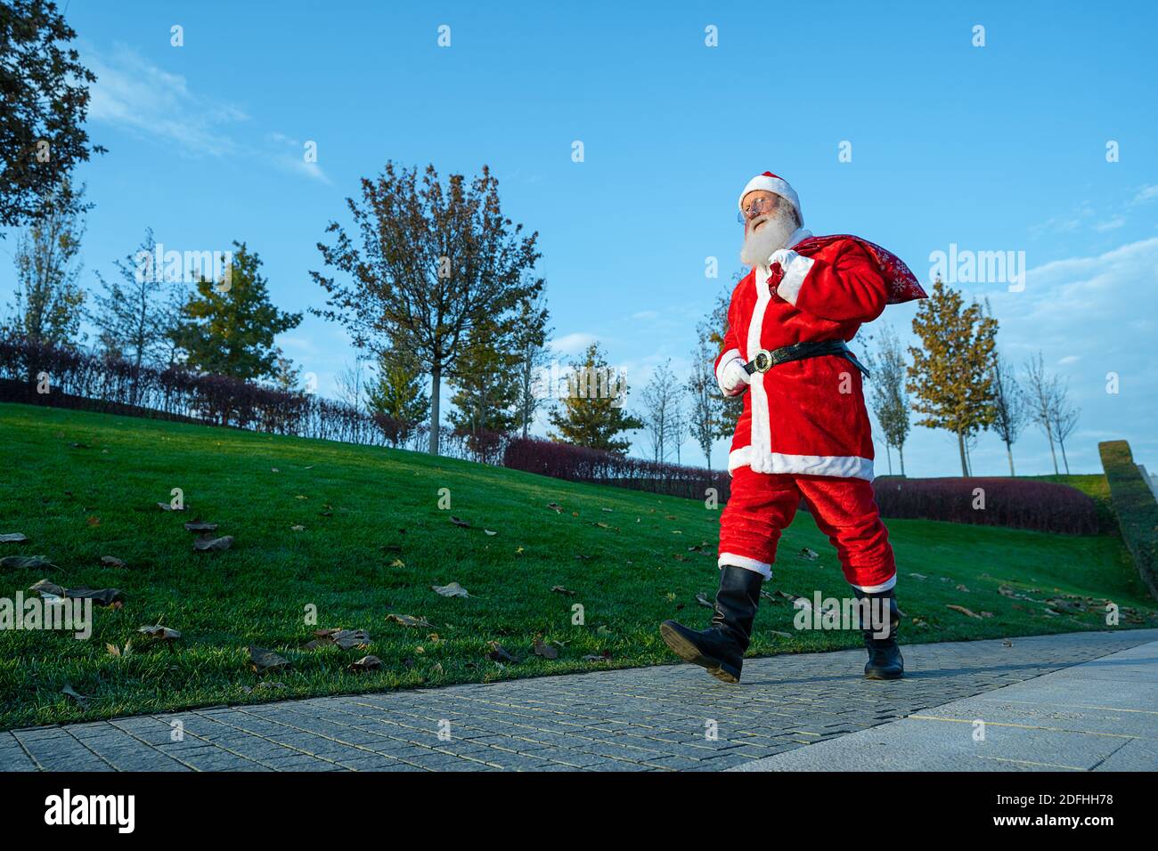 Divertente Babbo Natale che cammina lungo la strada con una borsa di regali Foto Stock