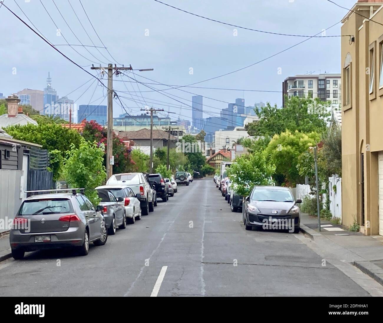 La strada residenziale della città interna nel sobborgo di Melbourne di Richmond con cottage singoli per famiglie, auto parcheggiate su entrambi i lati e il CBD della città sullo sfondo Foto Stock