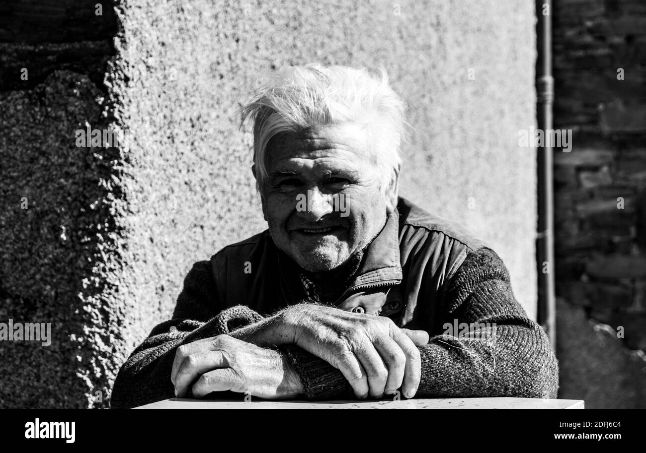 Vecchio contadino appoggiato su un muro per parlare con i visitatori Foto Stock
