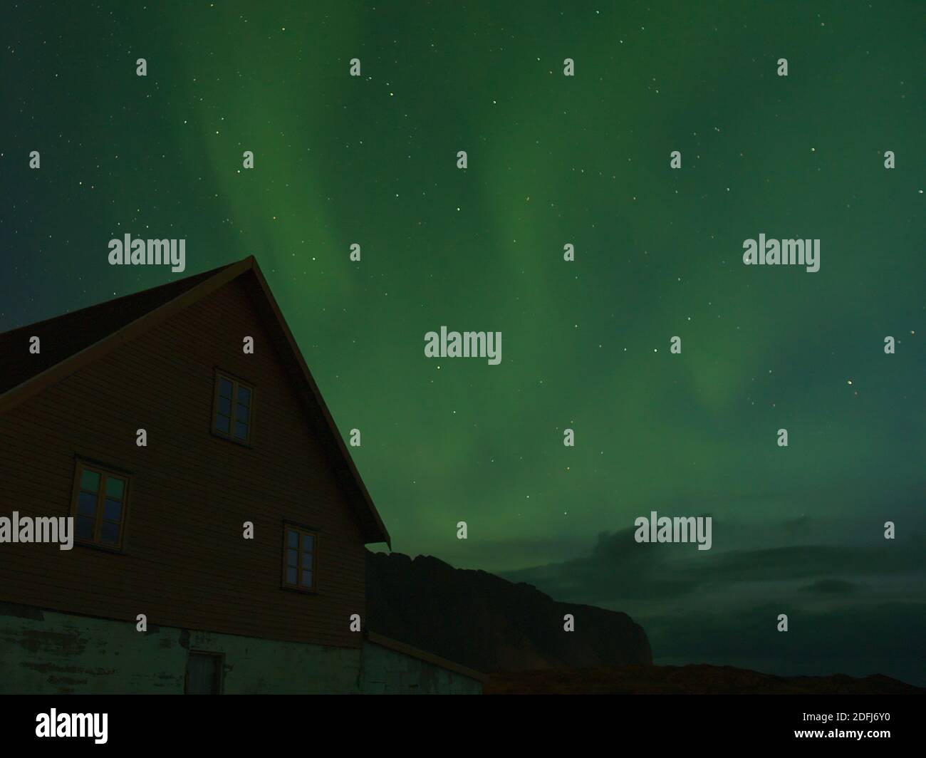 Bella vista del cielo notturno con luci polari lucide e luminose (aurora borealis) in colore verde sopra la vecchia casa e le sagome delle montagne in Norvegia. Foto Stock