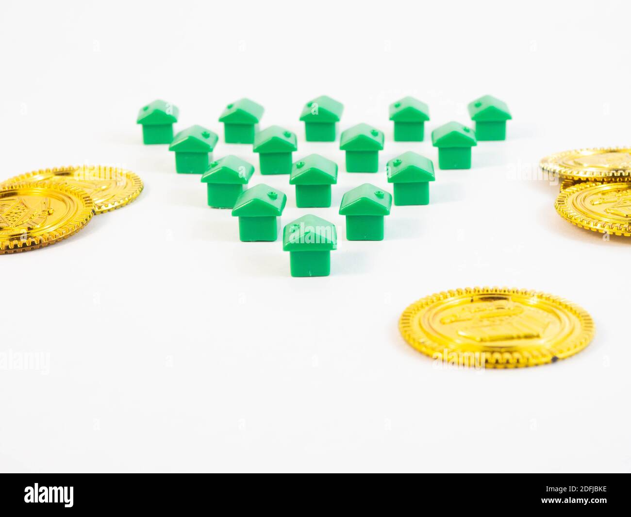 Pedine di colore verde a forma di casa con monete d'oro. Concetto intorno agli agenti immobiliari e immobiliari. Foto Stock