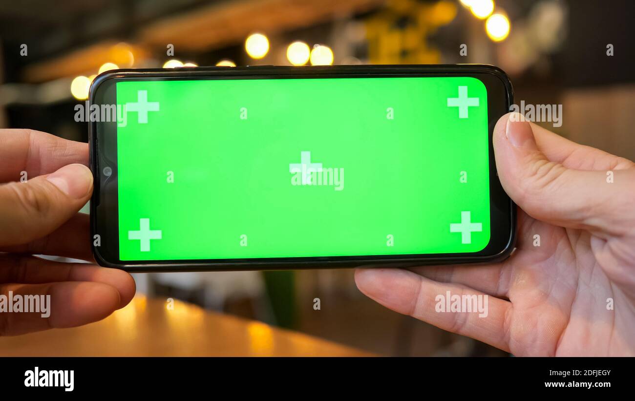 Mani maschili che tengono un telefono con uno schermo verde. Foto Stock