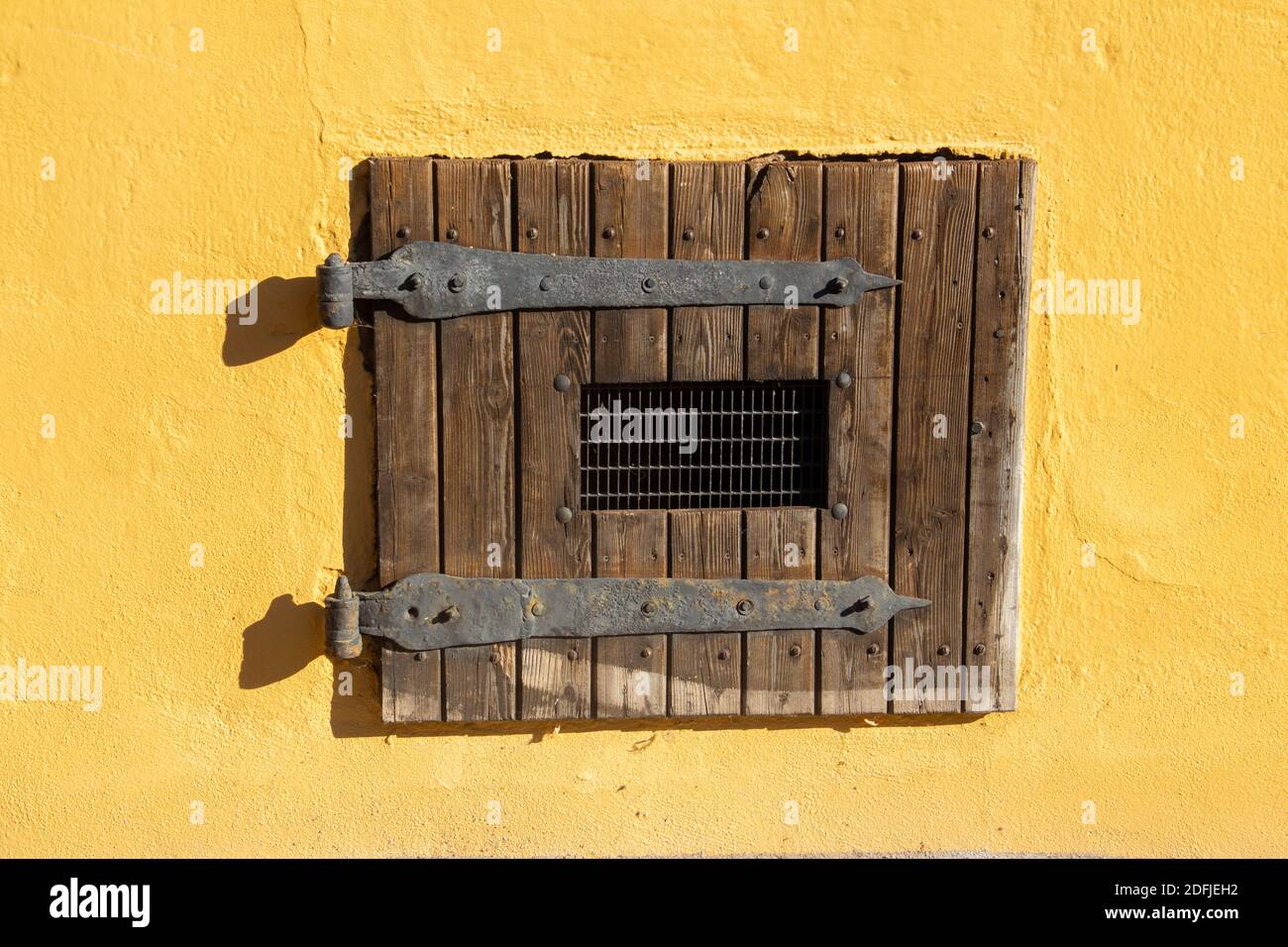 Vecchia serranda in legno vintage con griglia metallica su un giallo parete Foto Stock
