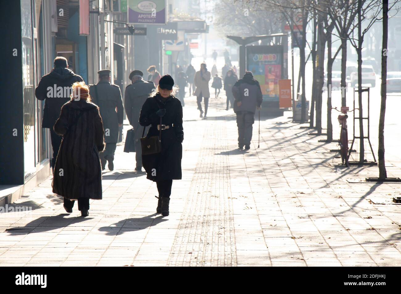 Belgrado, Serbia - 1 dicembre 2020: Una donna che cammina da sola sul marciapiede di una strada trafficata della città in un giorno di autunno freddo e soleggiato Foto Stock