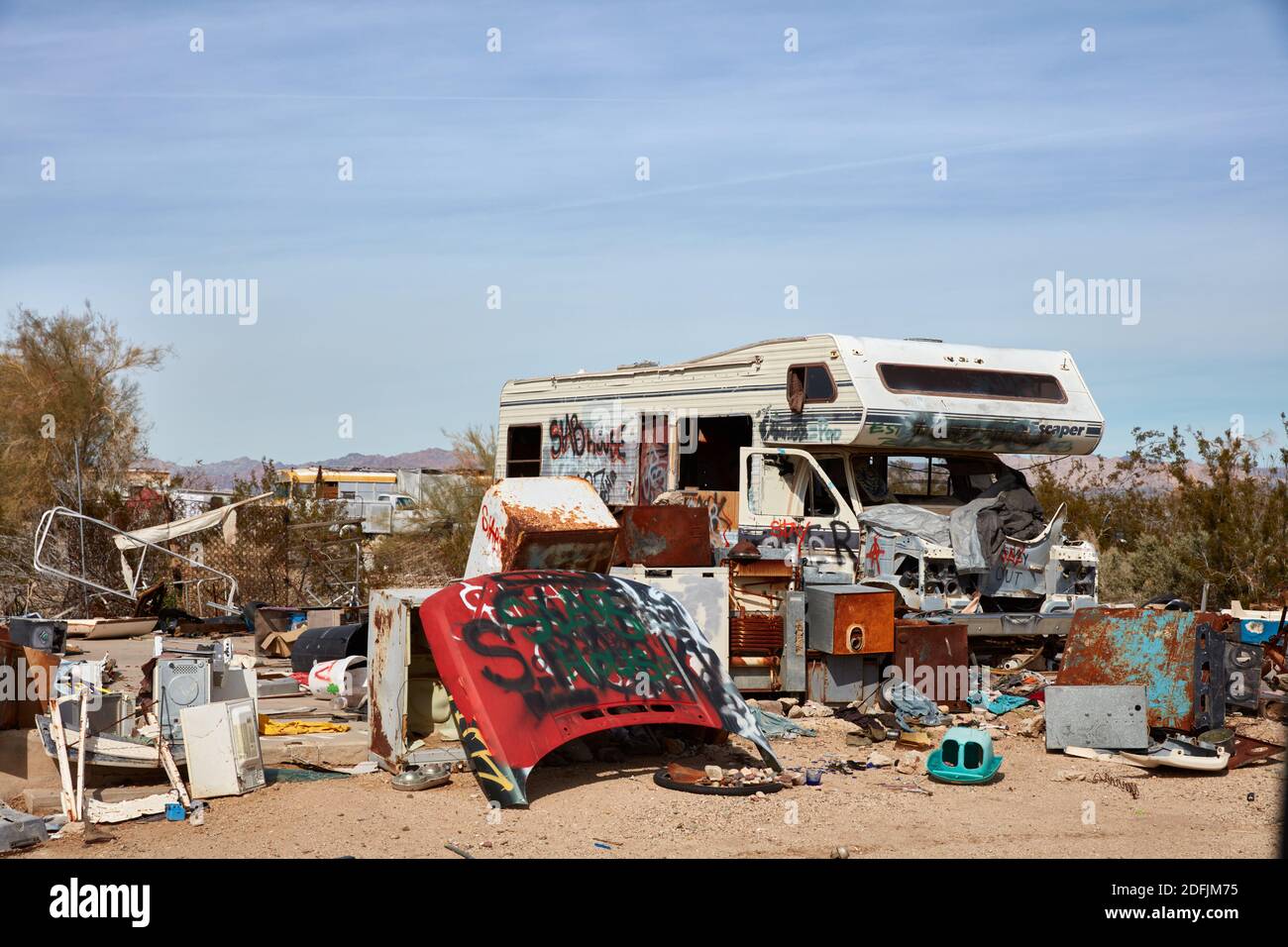 RV abbandonato seduto tra gli elettrodomestici scartati e le parti di auto a Slab City, California Foto Stock