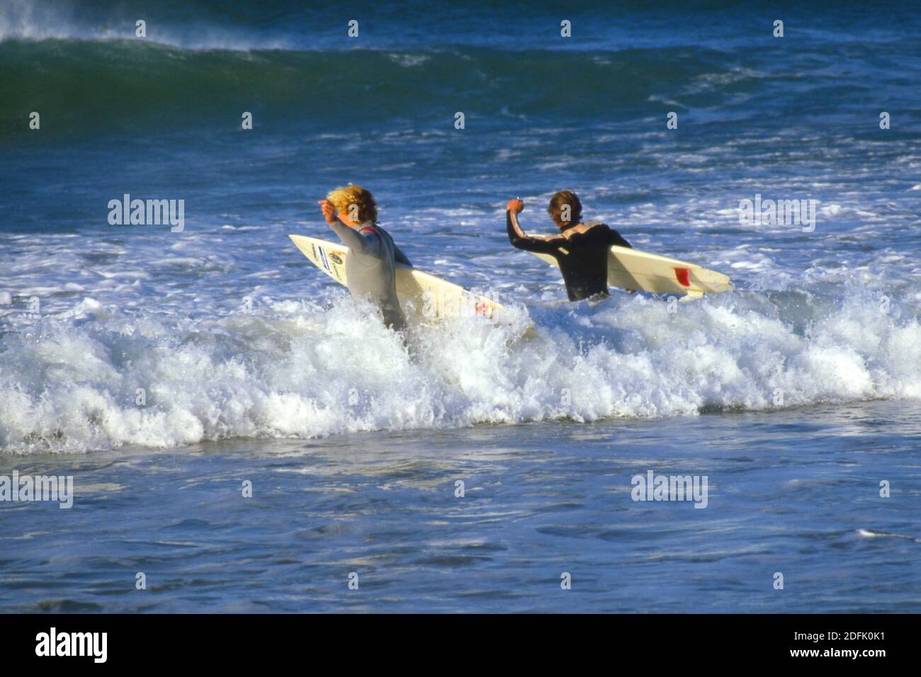 Due giovani che entrano in mare in mute umide, dotate di tavole da surf, Port Elizabeth, Sudafrica 1981 Foto Stock