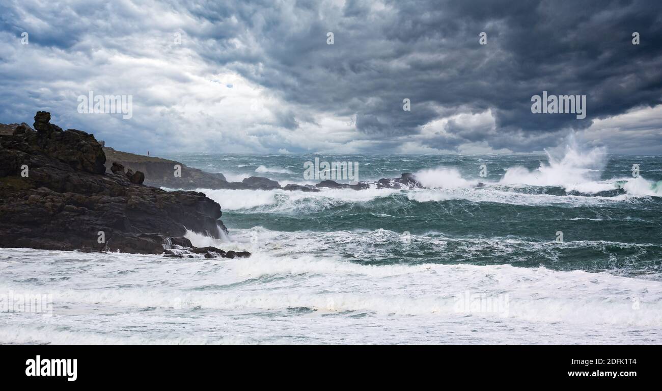 Mare drammatico e cielo tuoso con grandi onde che si infrangono su rocce Foto Stock