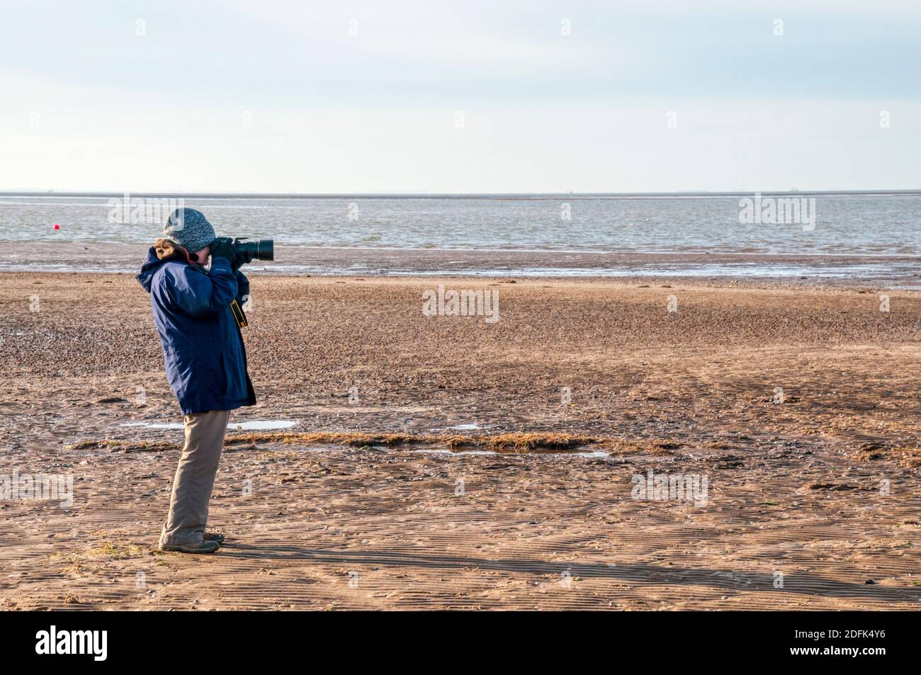 Donna che fotografa gli uccelli sulla riva orientale del Wash durante una giornata intensa ma fredda in inverno. Foto Stock