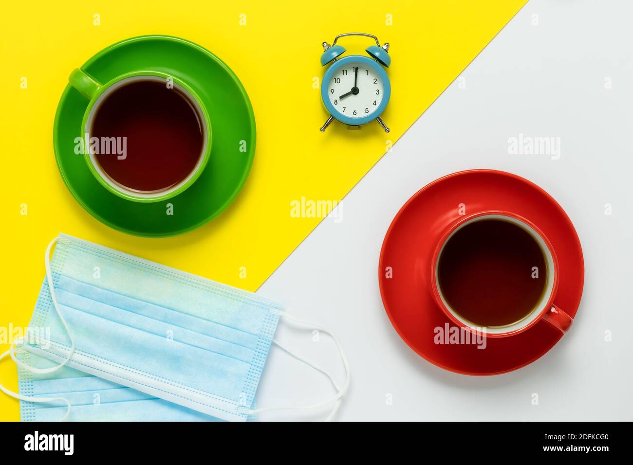 Tè bere. Ci sono due maschere mediche di protezione blu sul tavolo nel caffè. Due tazze in ceramica con piattini rossi e caffè su un giallo e bianco Foto Stock