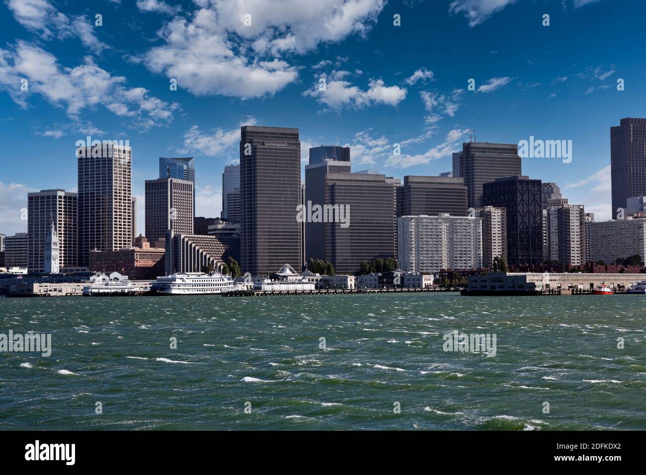 Vista dell'acqua soffiata dal vento e delle torri del centro con cielo parzialmente nuvoloso nella Baia di San Francisco. Foto Stock