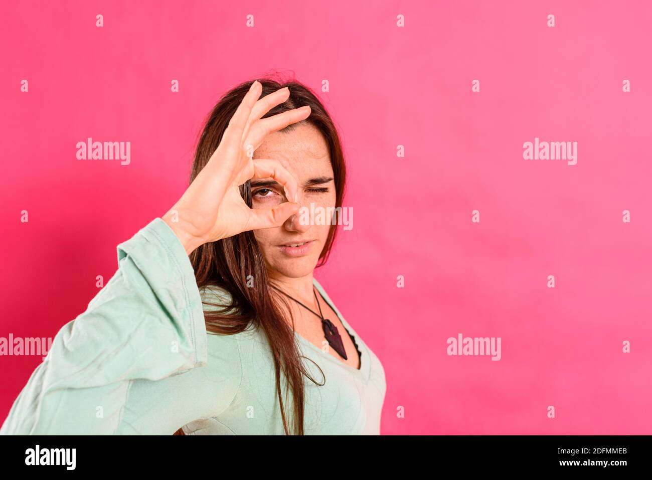 Donna usa le sue mani per mettere a fuoco la sua vista e guardare attraverso per tenere l'orologio, concetto di privacy isolato sullo sfondo. Foto Stock