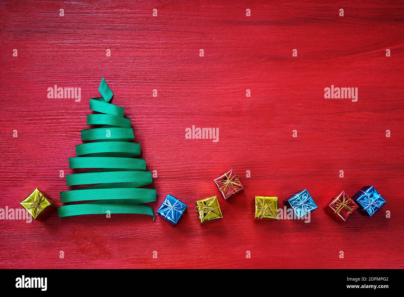 Albero di Natale fatto da nastro verde con piccoli regali su sfondo rosso. Foto Stock