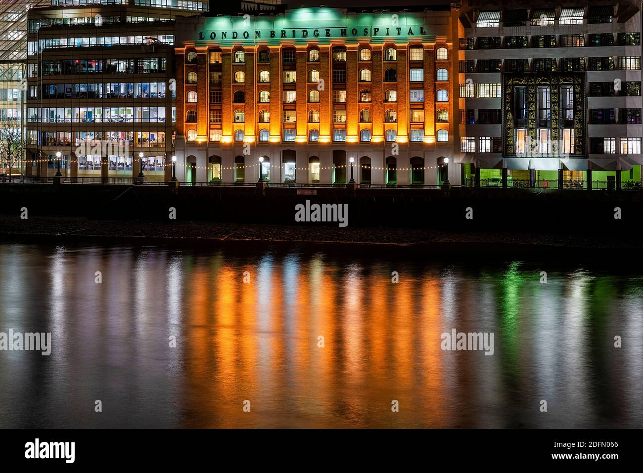Londra, UK - Gen 2020: London Bridge Hospital illuminato di notte accanto ai moderni edifici degli uffici, che si riflettono nel fiume Tamigi Foto Stock