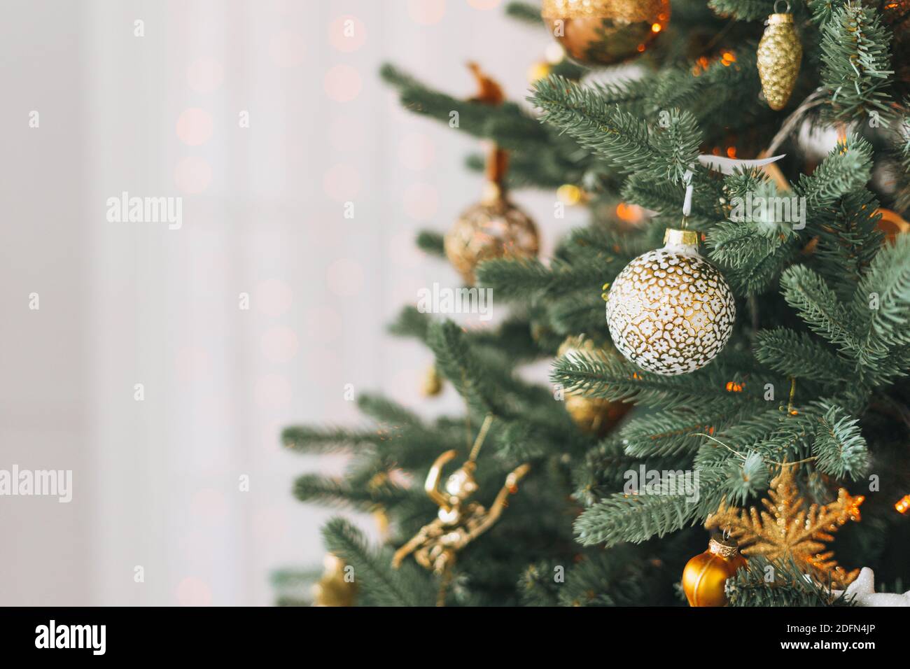 Albero di Natale decorato in giocattoli dorati e bianchi con luci sfondo bokeh testurizzato Foto Stock