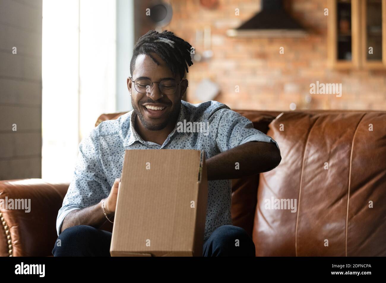 Sorridente giovane afroamericano disimballare il pacco. Foto Stock