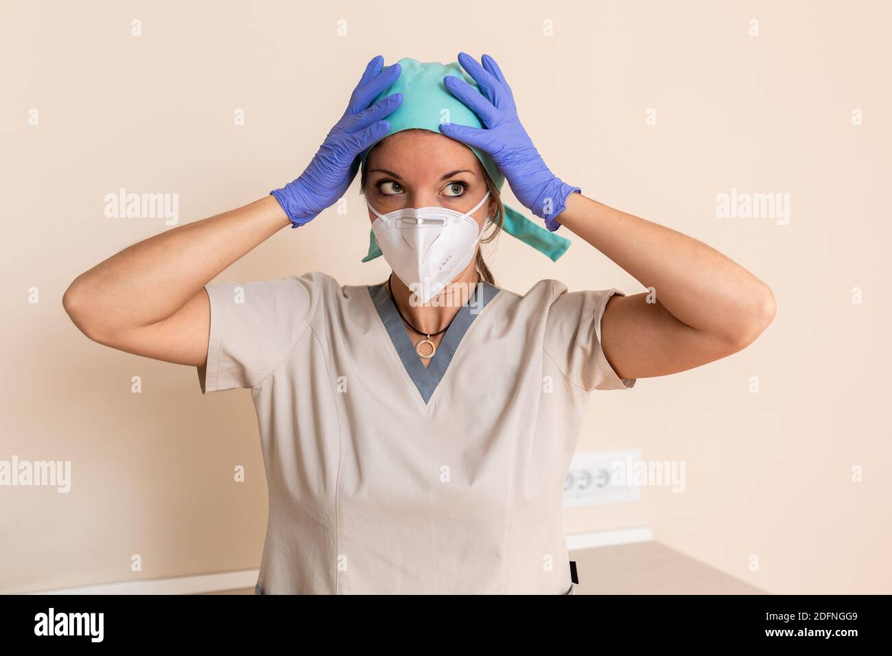 La ragazza dell'operatrice sanitaria è vestita con uniforme protettiva, cappuccio chirurgico, guanti in lattice e maschera Foto Stock