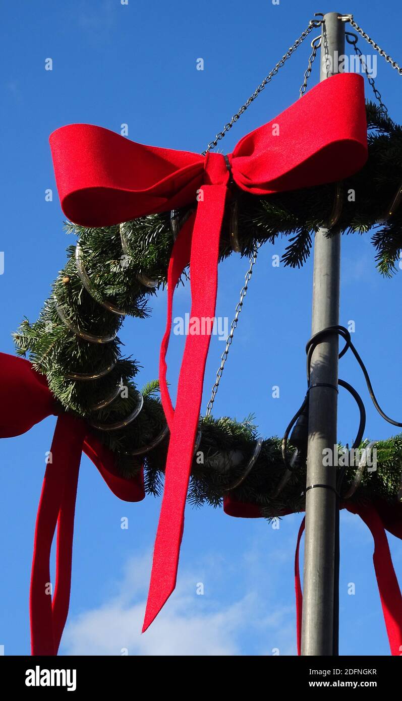 Dettaglio di una corona natalizia con rami di abete e nastri rossi su un palo. Cielo blu come sfondo. Foto Stock
