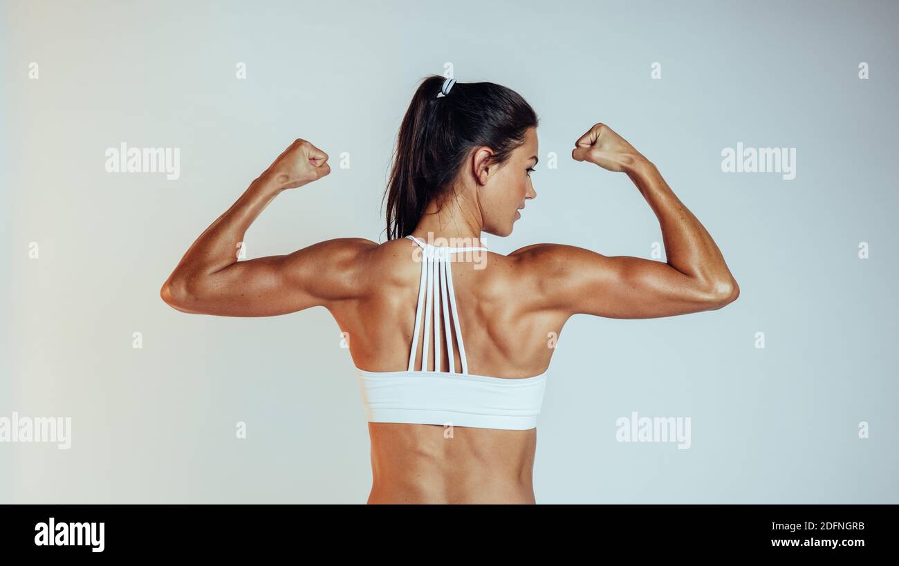 Donna atletica muscolare in piedi su sfondo bianco. Vista posteriore dell'atleta FIT che mostra i muscoli. Foto Stock