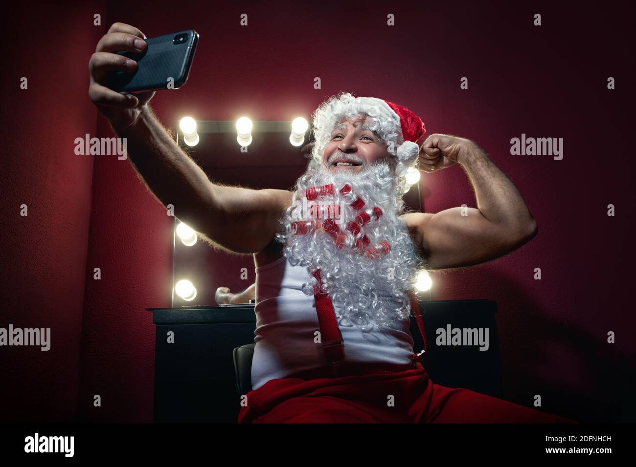 Narcisistico Babbo Natale sta facendo selfie con la fotocamera del telefono cellulare in uno spogliatoio Foto Stock