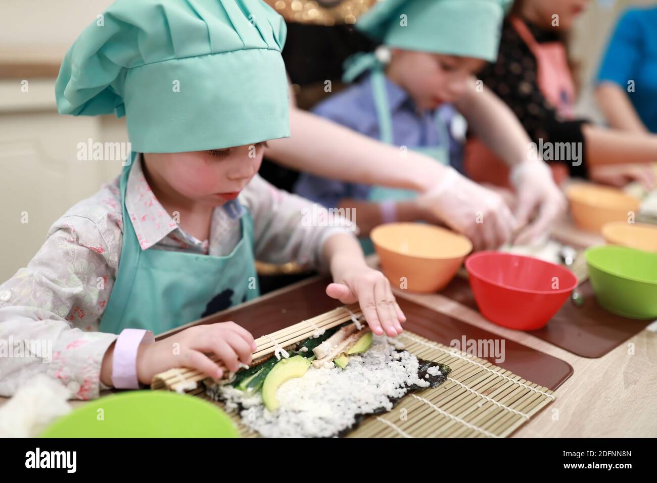 Il ragazzo sta rotolando il tappetino sopra il sushi alla lezione di cucina Foto Stock