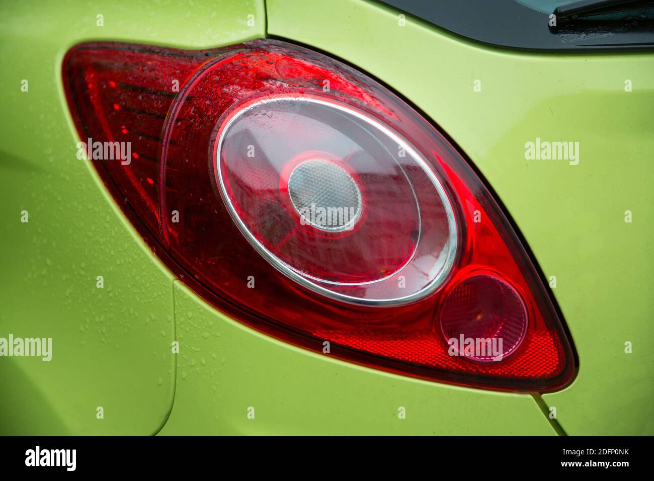 Vista ravvicinata dell'elegante luce di posizione posteriore dell'auto verde coperta dalla pioggia Foto Stock
