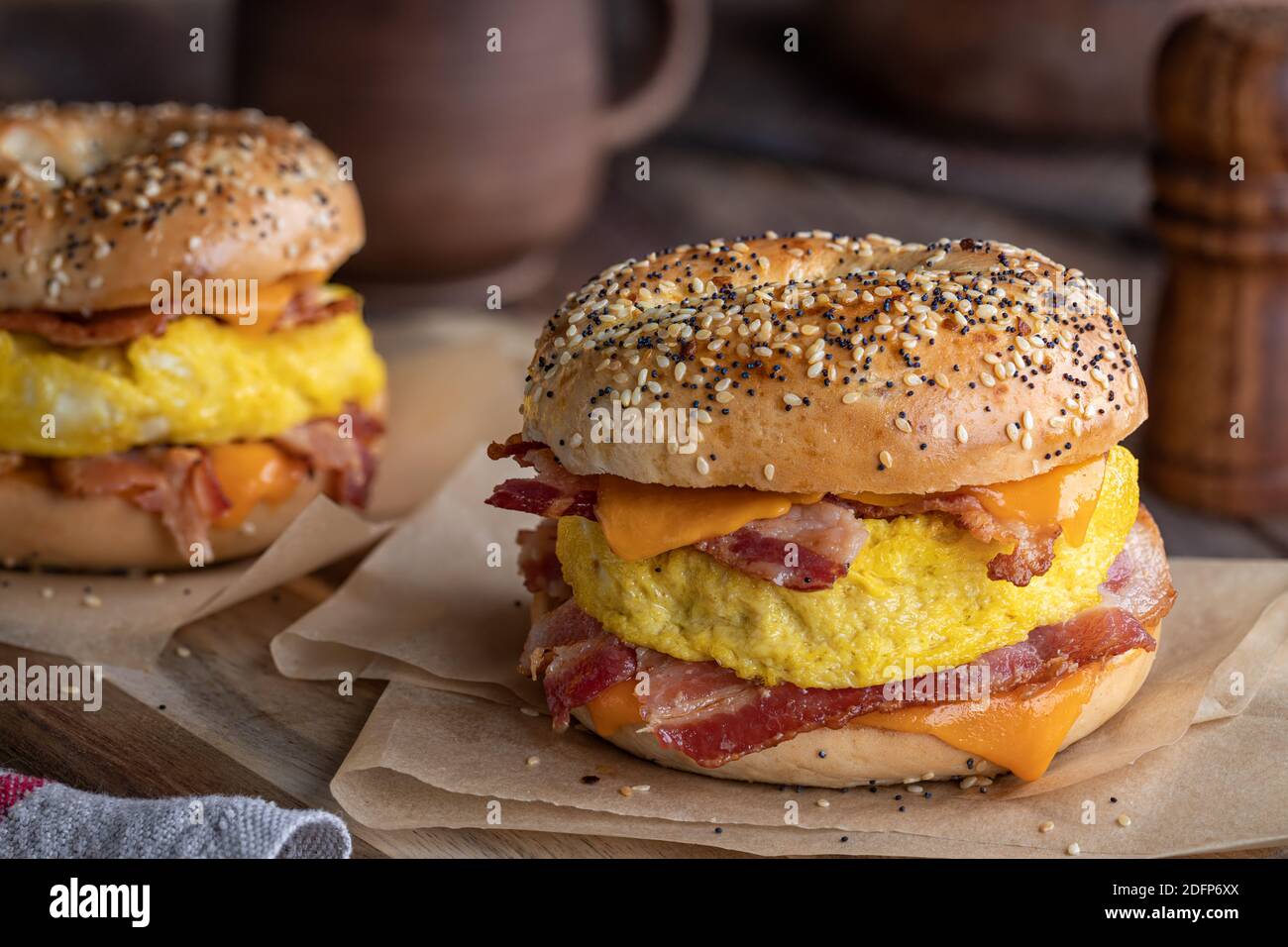 Sandwich con bagel e pancetta, uova e formaggio cheddar su un rustico tavolo di legno Foto Stock