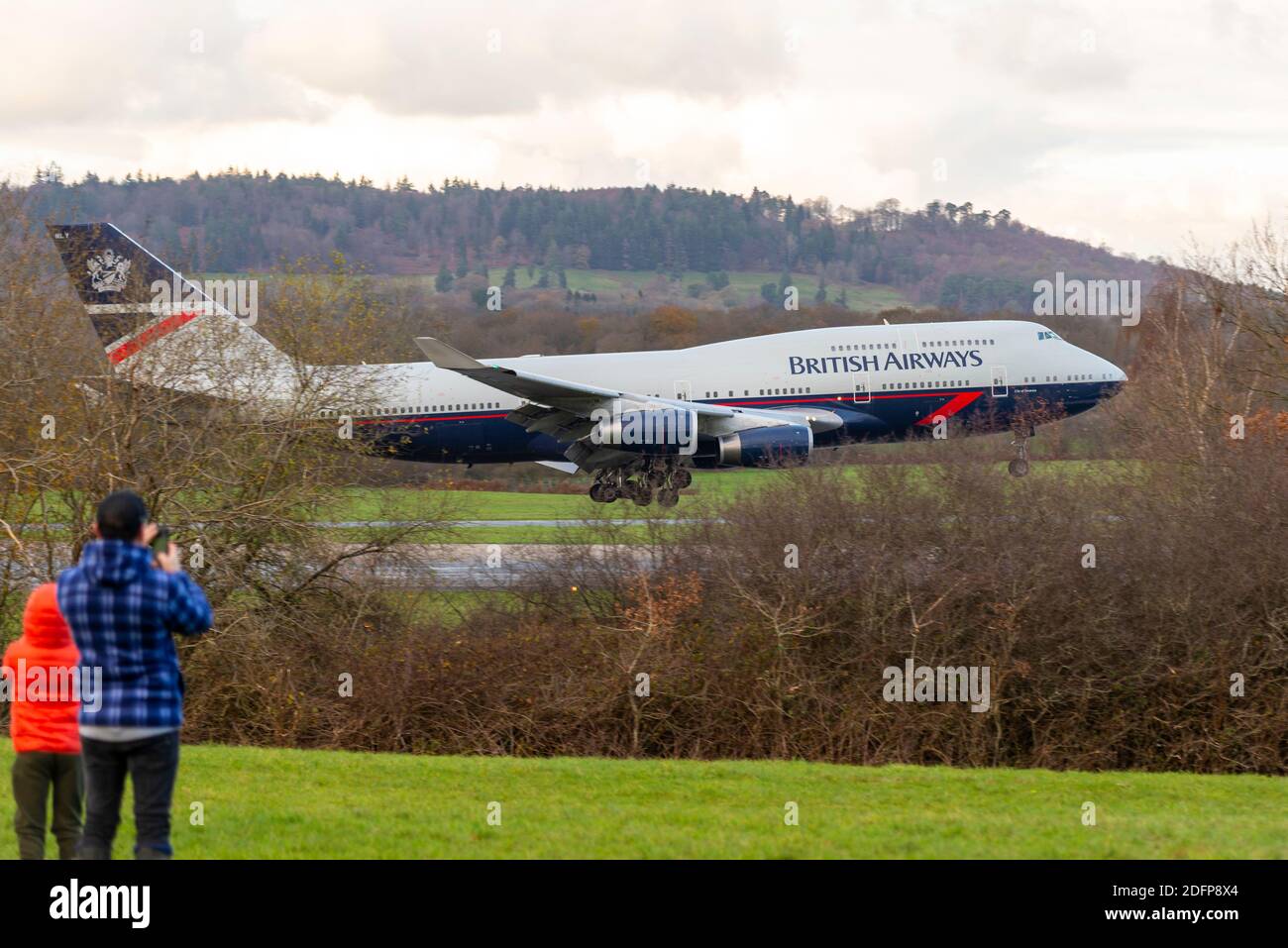 Volo finale dell'aereo Jumbo Jet Boeing 747 della British Airways G-BNLY in centenario retrò Landor schema di vernice atterraggio a Dunsfold con padre e bambino Foto Stock