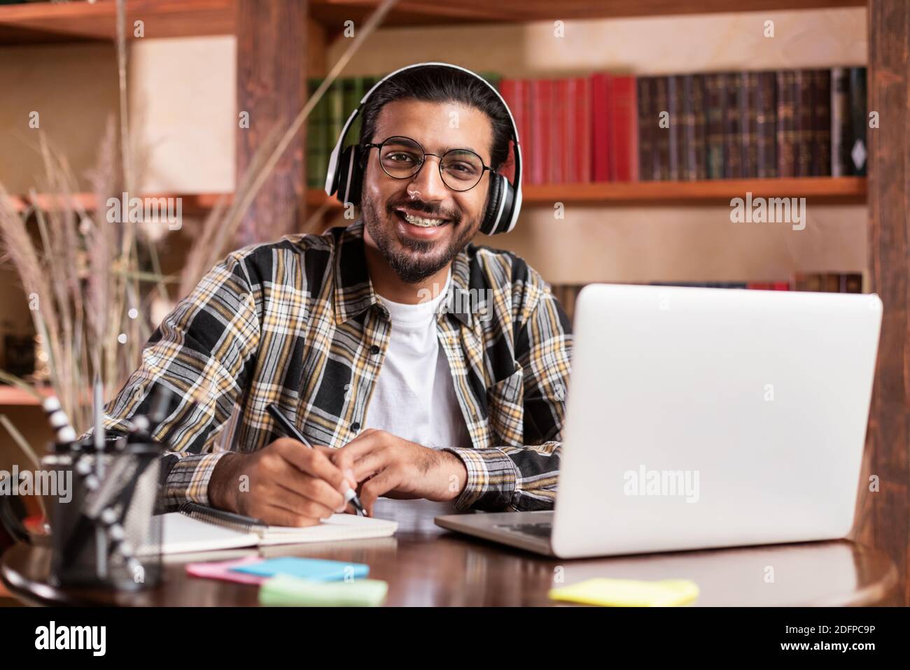 Indiano studente Guy in posa al laptop Learning Online in Biblioteca Foto Stock