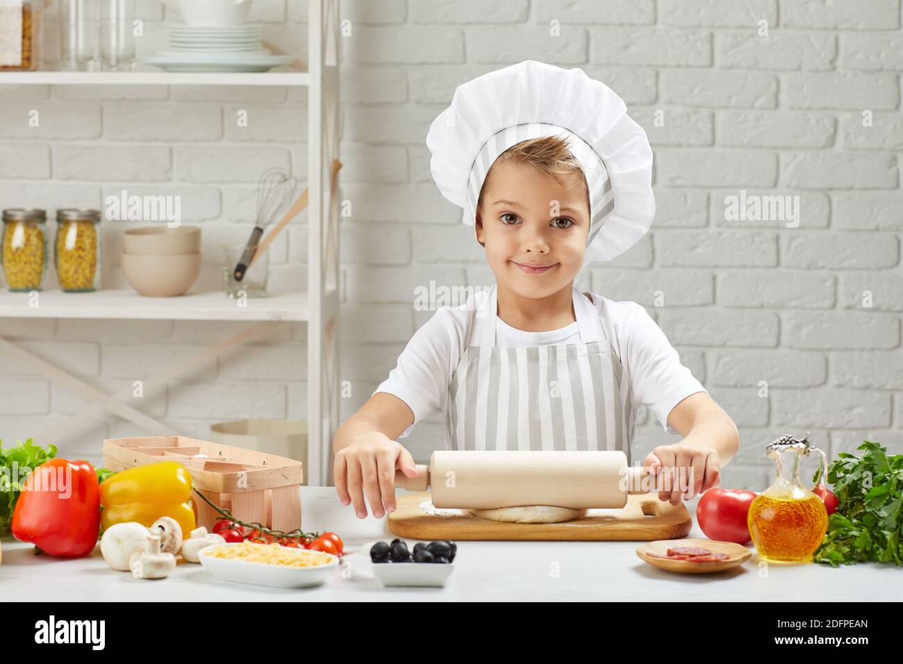 bambino piccolo in cappello chef e un grembiule arrotolato fuori l'impasto  in cucina Foto stock - Alamy