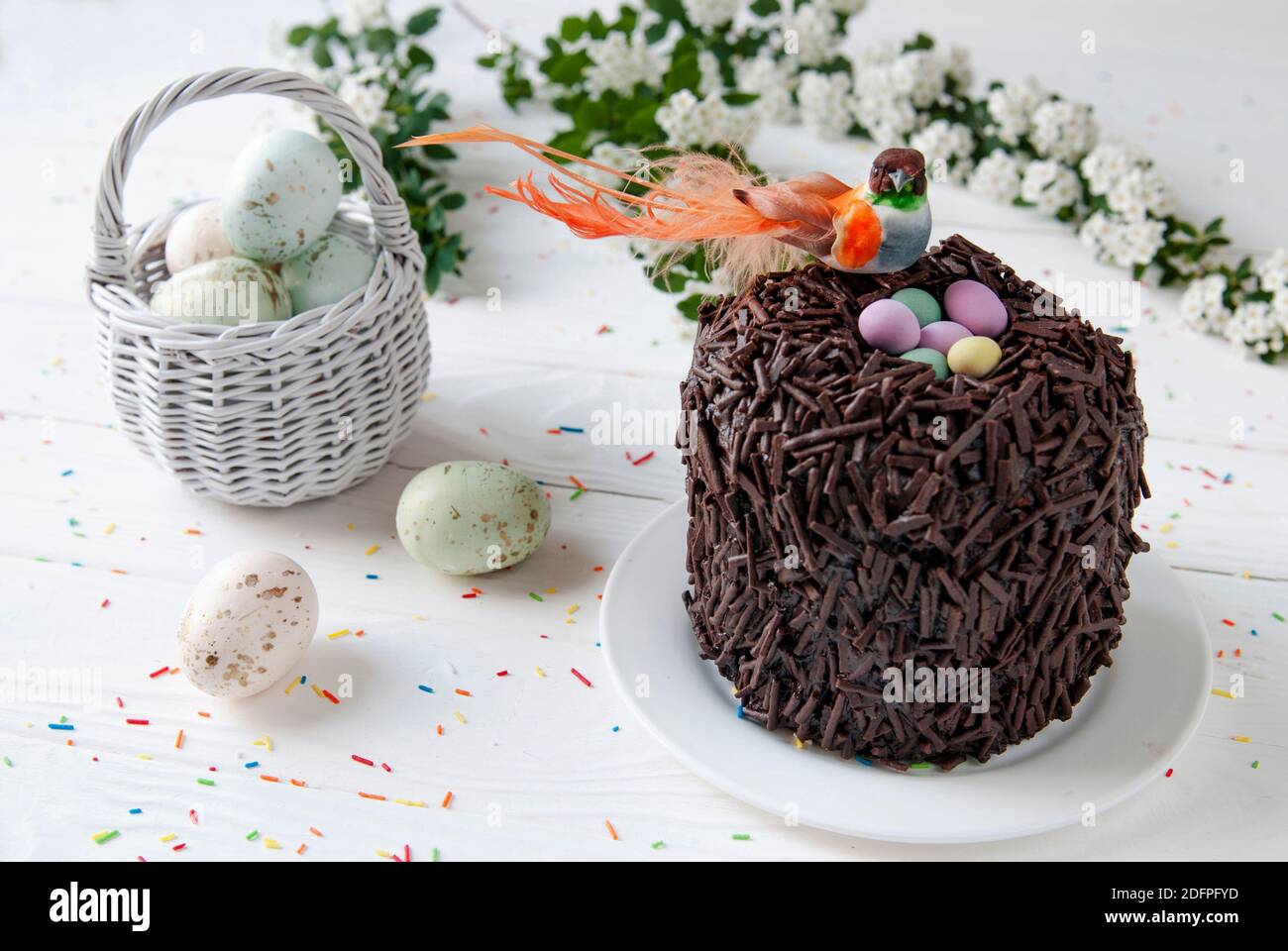 Torta di cioccolato di Pasqua e uccello seduto nel nido. Piccolo uccello arancione, uova colorate e cesto di vimini sullo sfondo degli arredi di Pasqua Foto Stock