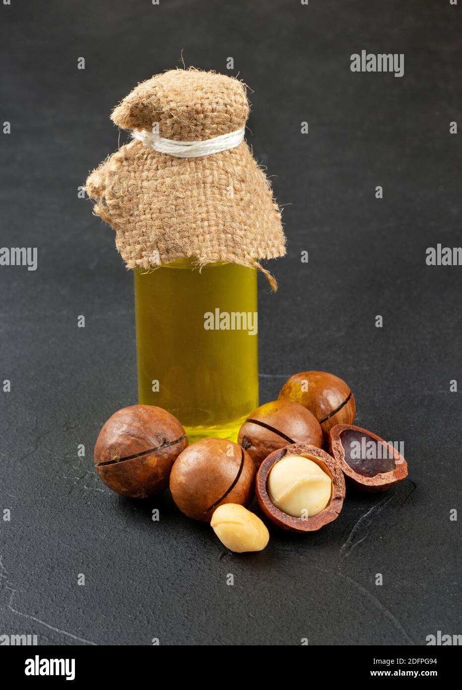 Oliare in una bottiglia con noci di macadamia al buio sfondo Foto Stock
