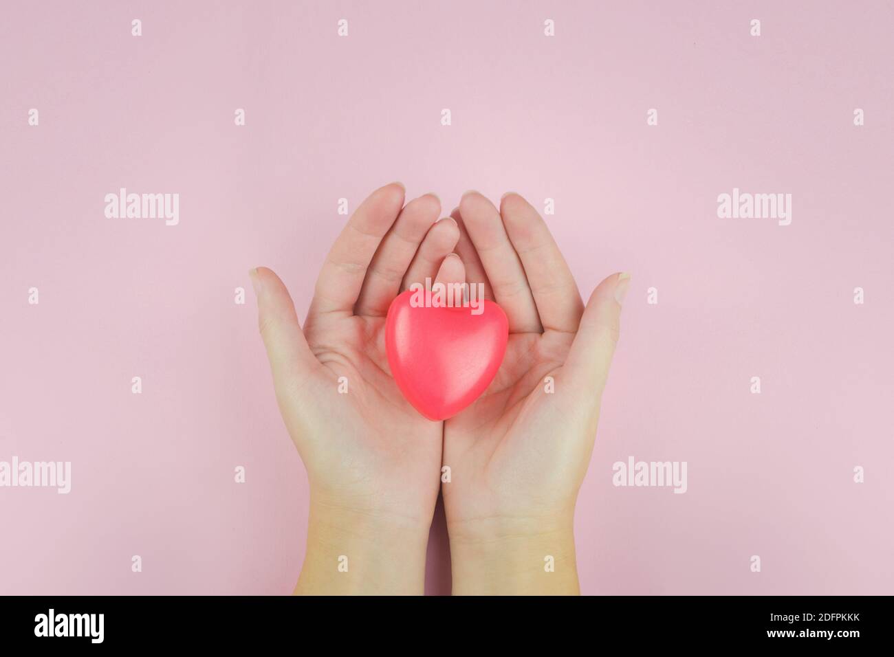 Donna che tiene la forma del cuore sopra sfondo rosa, cura di salute, donare e concetto di assicurazione della famiglia, giorno di salute del mondo, concetto di San Valentino Foto Stock