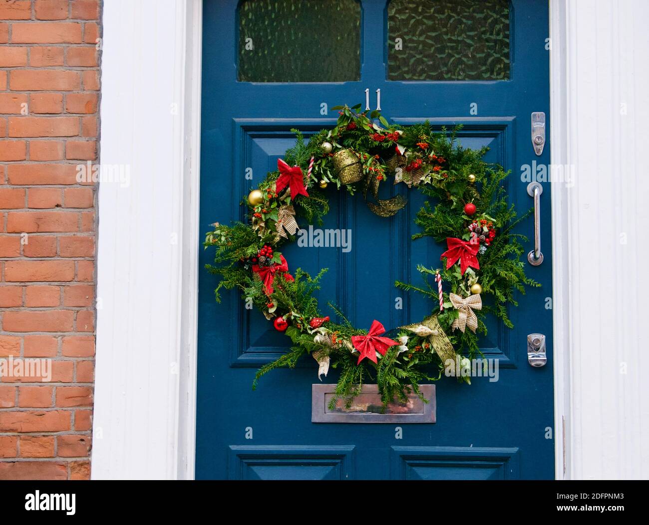 Corona dell'Avvento compostabile con foglie sempreverdi, nastri rossi e dorati e canne caramelle. Corona appesa su una casa blu porta di fronte a Highgate, Londra. Foto Stock