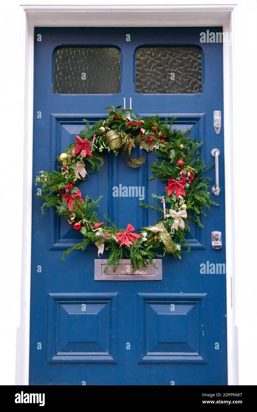 Corona dell'Avvento compostabile con foglie sempreverdi, nastri rossi e dorati e canne caramelle. Corona appesa su una casa blu porta di fronte a Highgate, Londra. Foto Stock