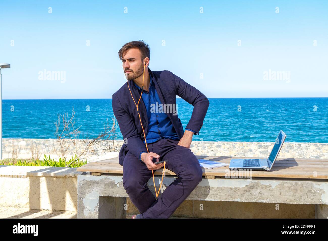 Giovane uomo che usa il telefono cellulare vicino all'oceano. Bell'uomo che ascolta con gli auricolari mobili iphone al parco della città wi-fi cellulare dati servizio duri cellulare Foto Stock