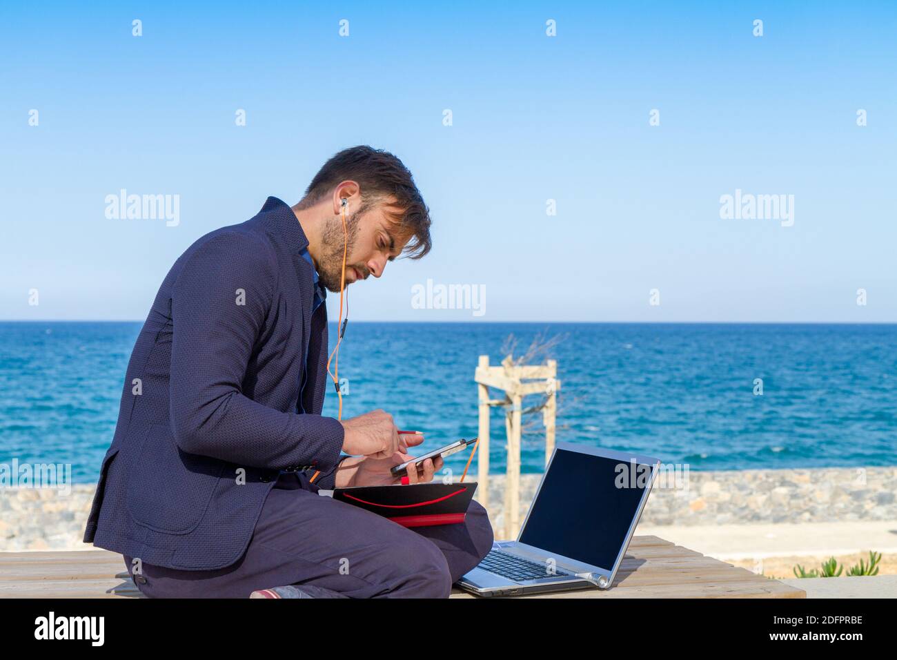 Giovane uomo che usa il telefono cellulare vicino all'oceano. Bell'uomo che ascolta con gli auricolari mobili iphone al parco della città wi-fi cellulare dati servizio duri cellulare Foto Stock