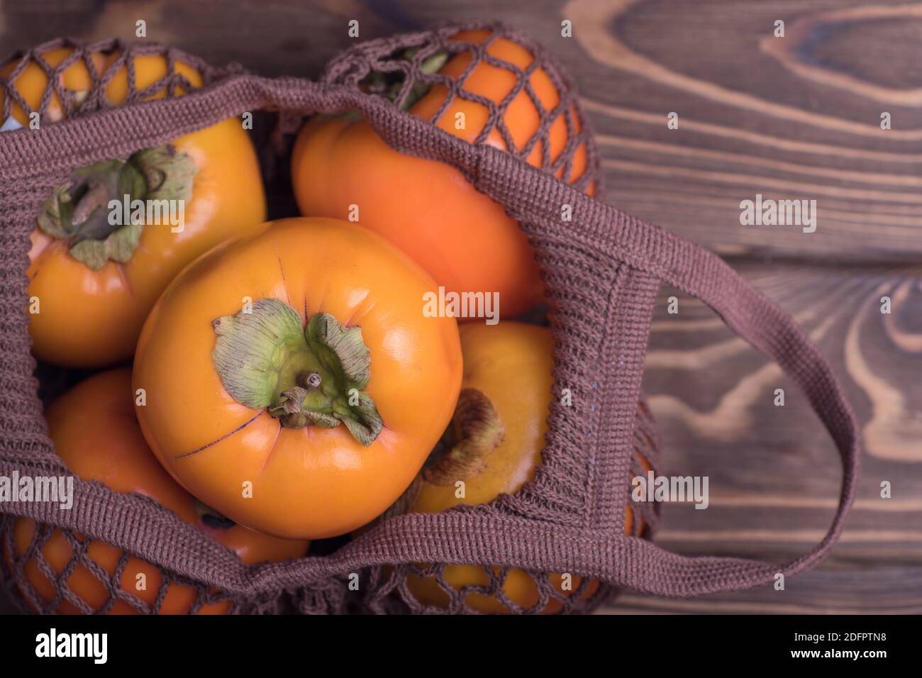 Ravvicinato di persimmon arancio maturo Fruit.Close-up di persimmons fresco in una borsa a corda su uno sfondo di legno. Zero ovest. Foto Stock