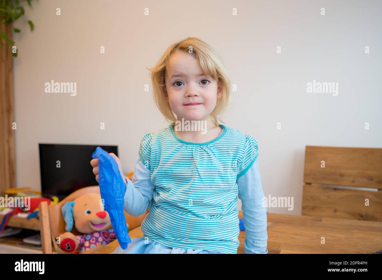 Ragazza bionda carina che gioca con guanti di gomma medica a casa. Foto Stock