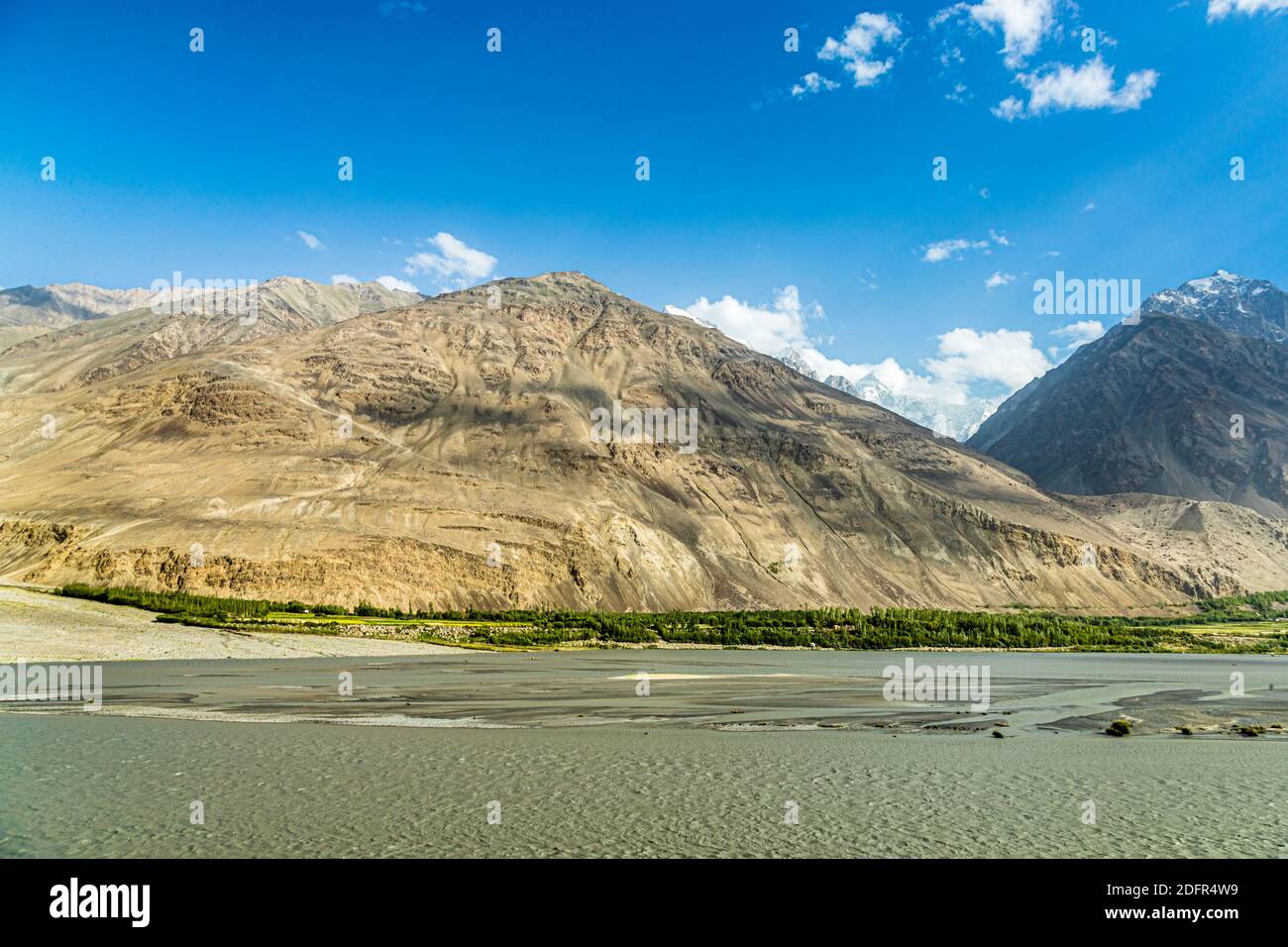 Strisce verdi lungo il fiume costeggiano l'ampio corso del fiume Panj vicino a Boibar, Tagikistan. Foto Stock