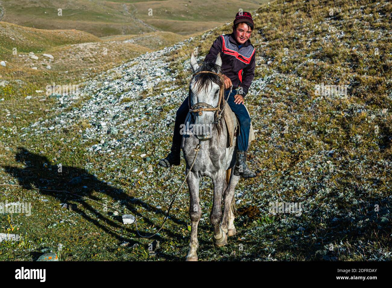 Giovane nomade Dschangube cavalca il suo cavallo lungo un pendio roccioso vicino ai laghi Tulpar-Kul nel Kirghizistan. Foto Stock