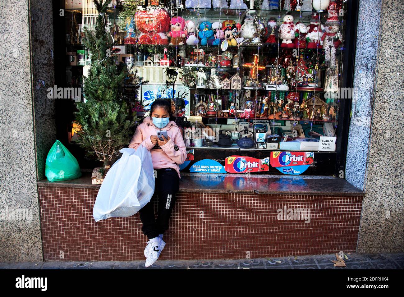 Giovane seduto fuori negozio giocare con il suo smartphone, Barcellona, Spagna. Foto Stock