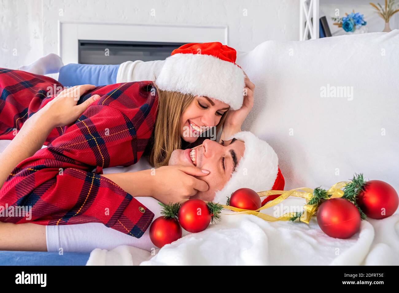 Ritratto di un uomo e di una donna con vista laterale sdraiati Un divano circondato da palle di Natale che indossano cappelli santa e. pigiami Foto Stock