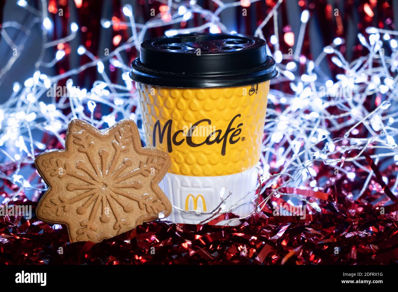 Primo piano della tazza McCafe gialla con pan di zenzero di fiocco di neve sullo sfondo festivo di Capodanno. Tinsel rosso e ghirlanda sullo sfondo. Kiev, Ucraina, Foto Stock