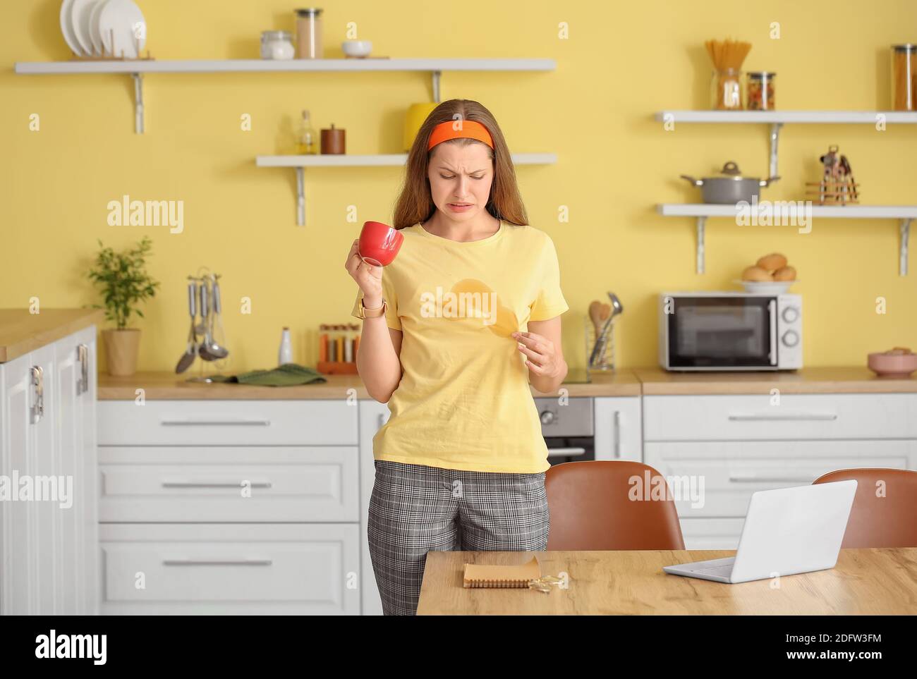 Giovane donna stressata con macchie di caffè sulla sua t-shirt dentro cucina Foto Stock
