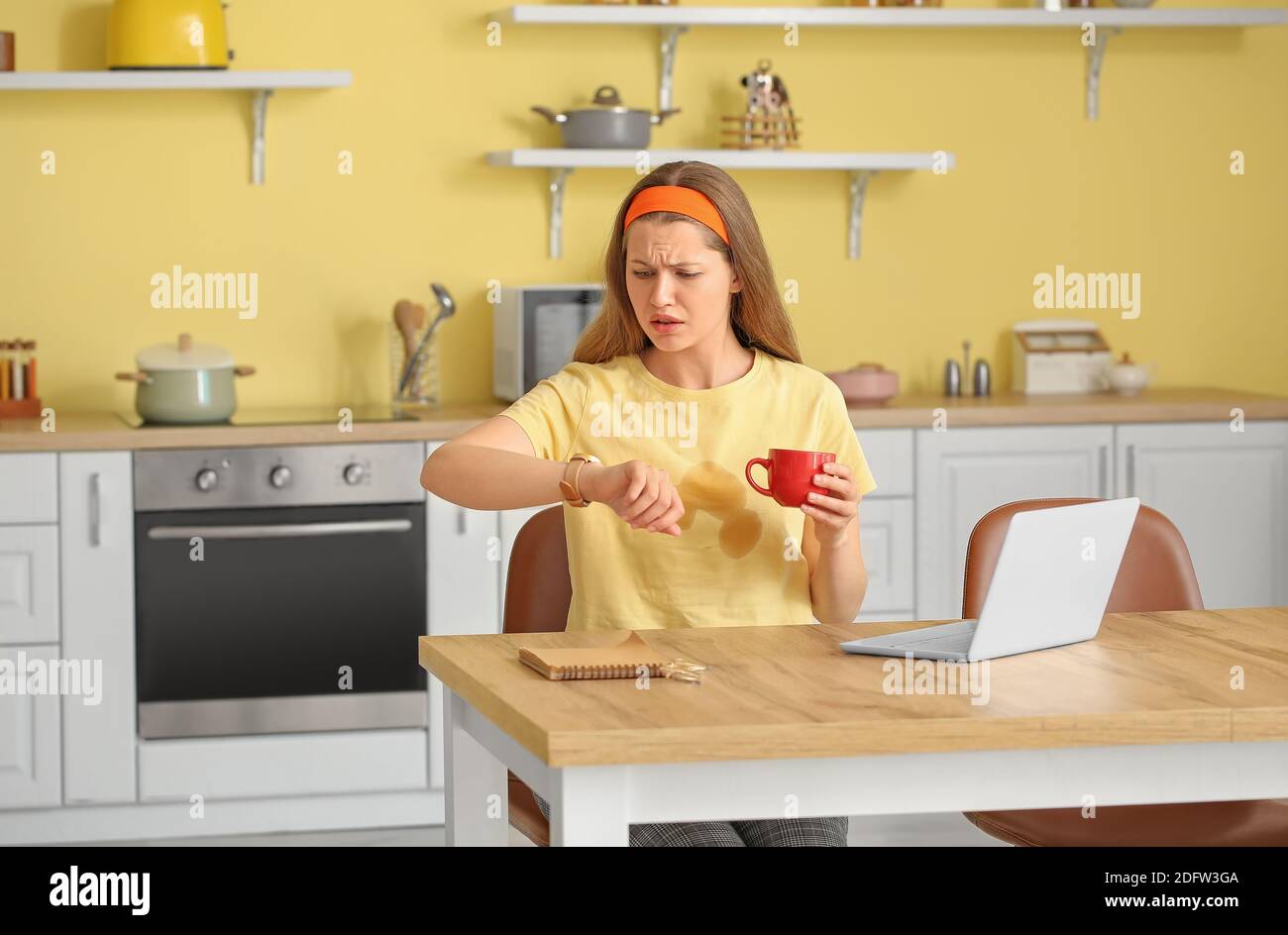 Giovane donna stressata con macchie di caffè sulla sua t-shirt dentro cucina Foto Stock